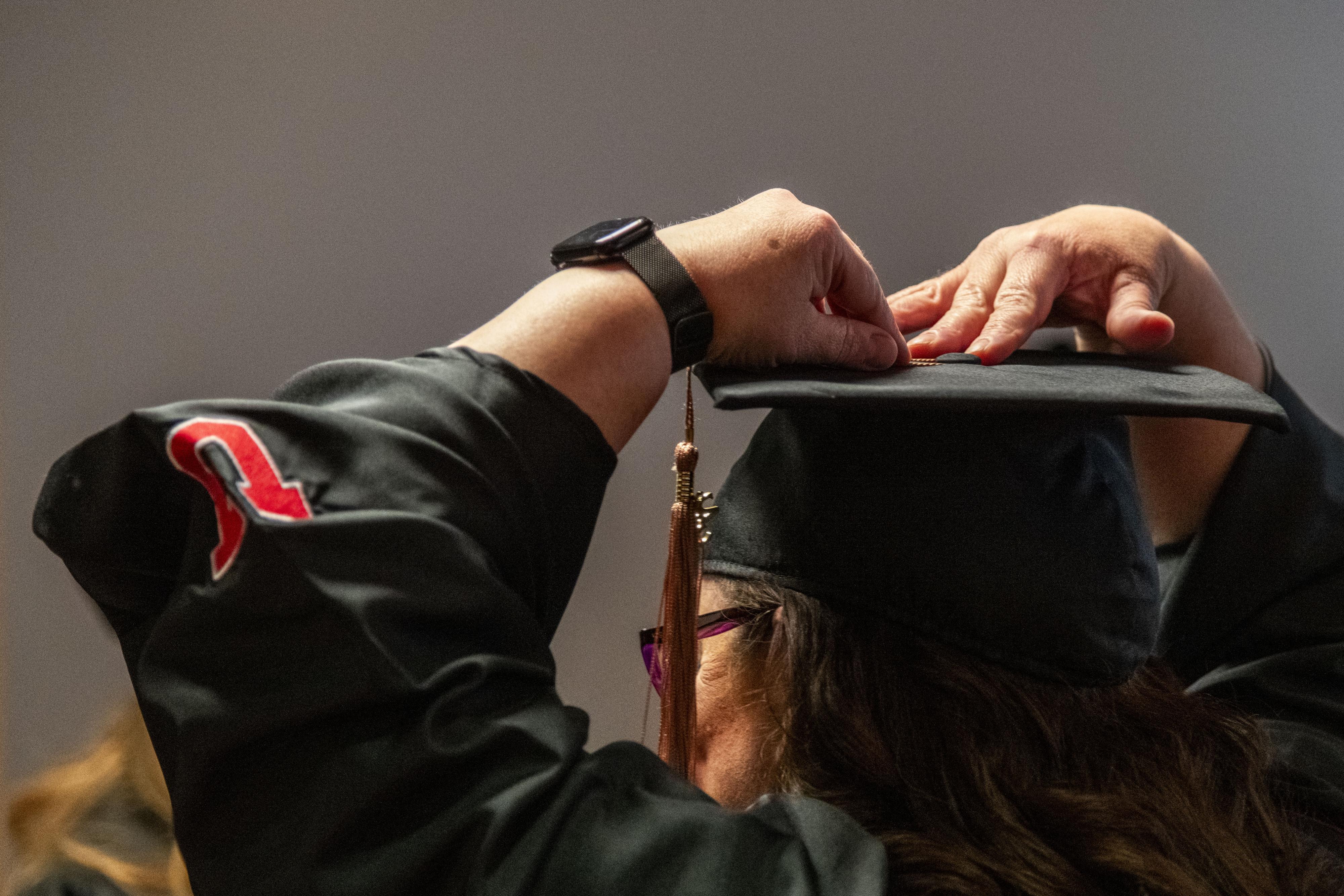 A graduate adjusts a tassel on top of a cap