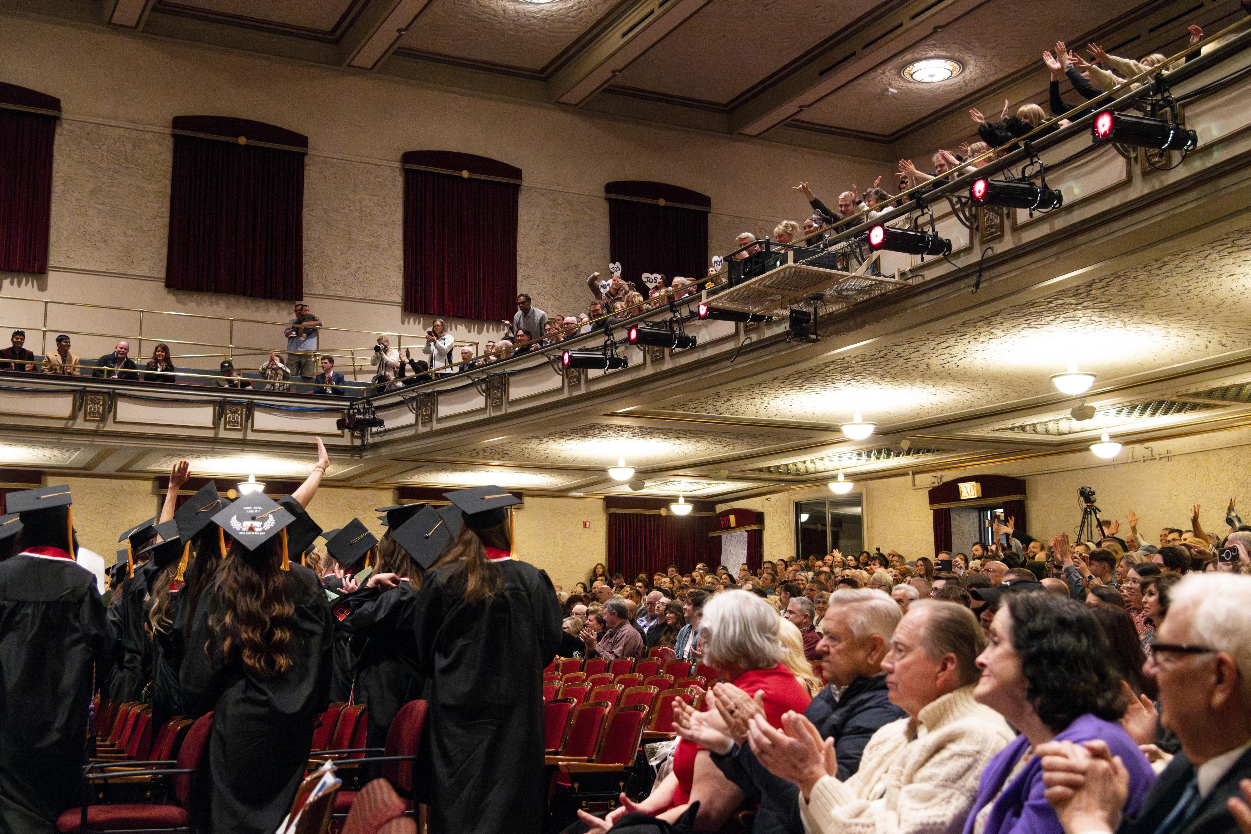 Graduates applaud towards supporters in the audience